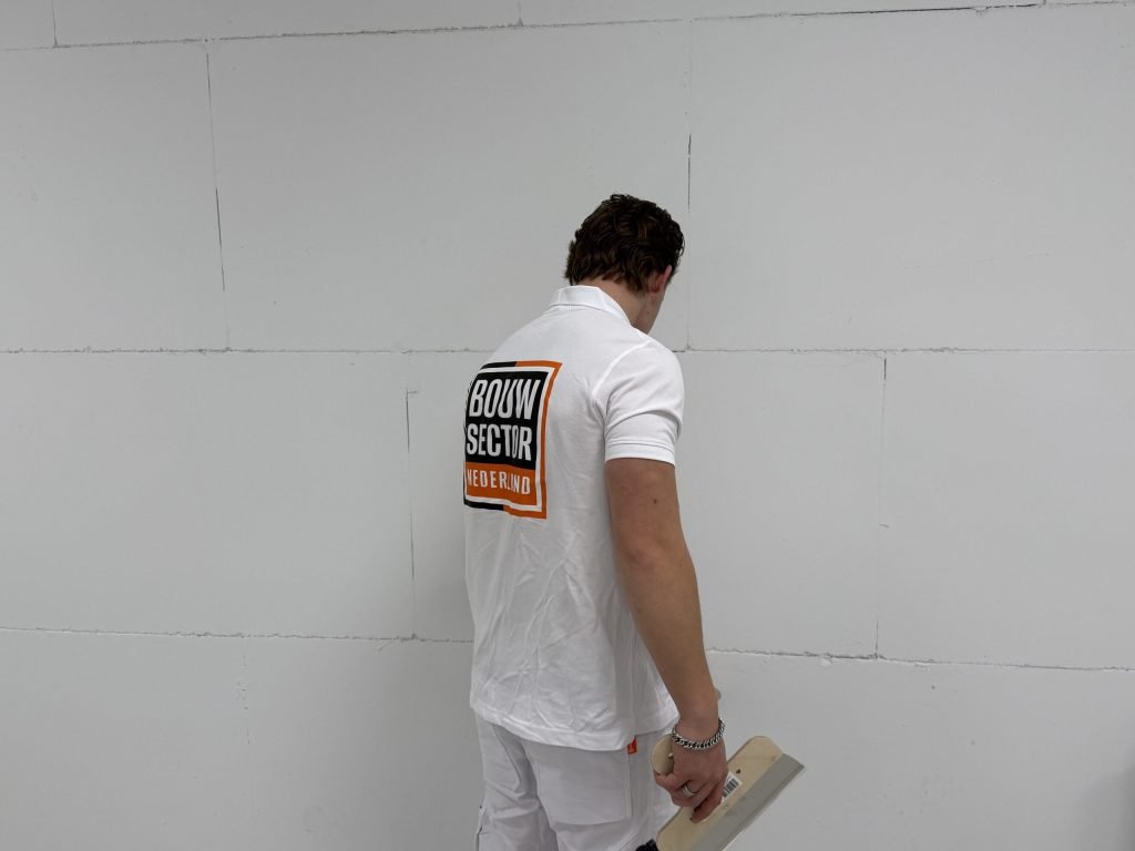 Stukadoor bekijkt met een plamuurmes in de hand een muur van blokken voordat hij gaat stucen