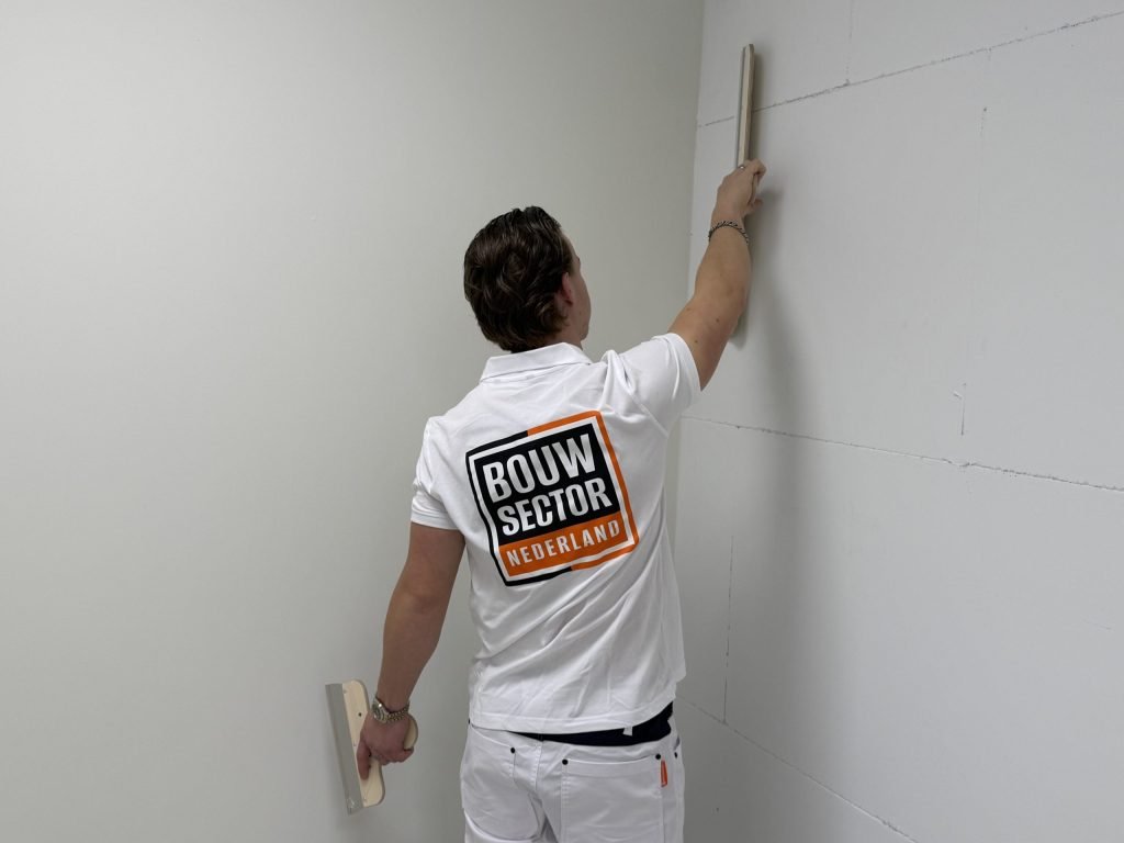 Stukadoor reikt in de hoek van een kamer met een spaan naar het bovenste deel van de wand