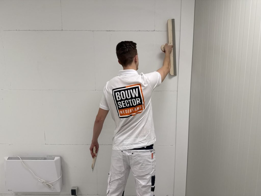 Vakman van Bouwsector Nederland zet een wand vlak met een spaan, van achteren gezien