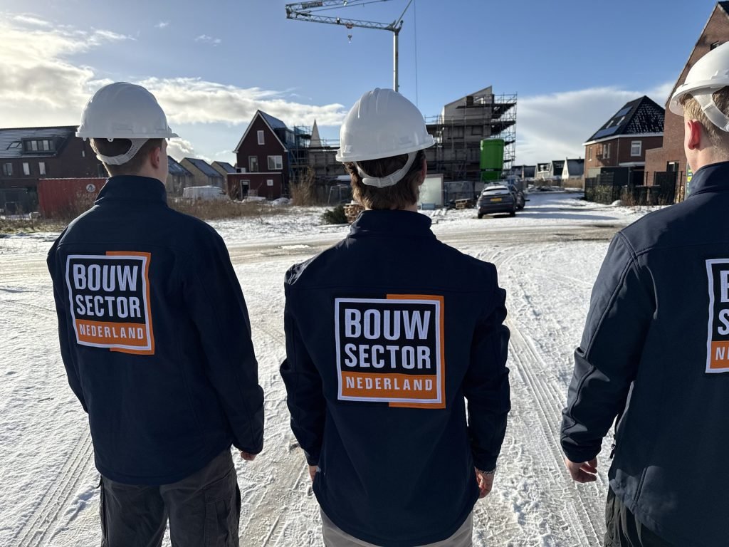 Drie medewerkers van Bouwsector Nederland met witte helm kijken naar woningen in aanbouw op een besneeuwd terrein