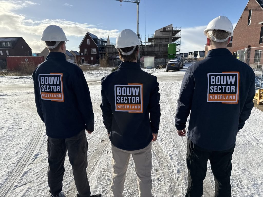 Drie vakmensen met witte helm en bedrijfsjas van Bouwsector Nederland op een besneeuwde bouwplaats